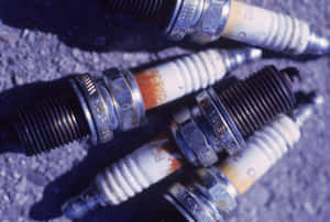 Worn spark plugs with orange deposits on gritty asphalt.