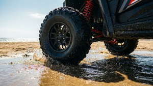 Veicolo fuoristrada nero che sguazza attraverso acqua oceanica su spiaggia sabbiosa.