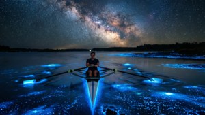 Remero solitario bajo la Vía Láctea con agua bioluminiscente, surrealista y mágico