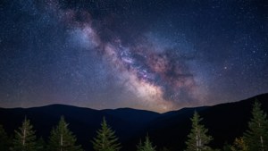 En klar nattehimmel fyldt med stjerner over silhuetten af bjergrygge.
