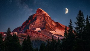 Un majestueux sommet de montagne rouge illuminé par le clair de lune sous un ciel nocturne étoilé.