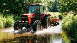 Traktor Massey Ferguson memercik melalui sungai kecil di musim panas