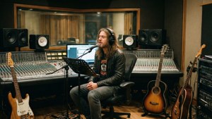 Musiker spiller inn vokal i et studio med gitarer og miksebord.