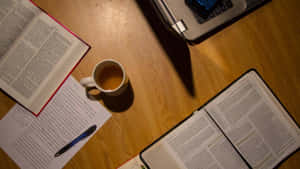 Schreibtisch mit offenen Büchern, Kaffeetasse, Laptop und handschriftlichen Notizen bei warmem Licht. — Notebook Wallpaper