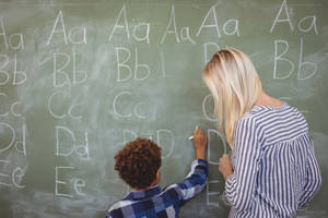 Enseignant et enfant écrivant des lettres sur un tableau dans une salle de classe.