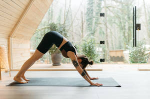 Kvinna utövar yoga inomhus med skogsutsikt genom glasdörrar. — Pilates Bilder