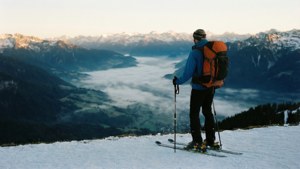 Uno sciatore si trova sulla vetta mentre l'alba irrompe su una valle nebbiosa.