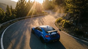 En blå Gran Turismo-bil med udsigt over en bjergslyngning ved solnedgang.