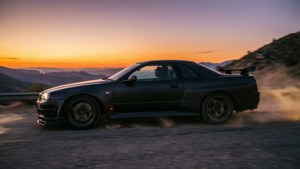 Un GTR R33 negro mate acelerando en una carretera de montaña al atardecer con iluminación dramática.