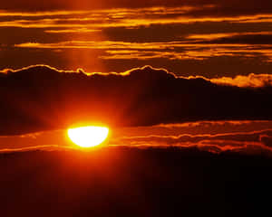 A vibrant orange sunset with sun partially obscured by clouds. — Sunset Hues Wallpaper