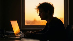 Silhuet af en coder ved et skrivebord med solnedgangslys og laptop-glød