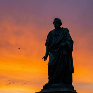 Een minimalistische achtergrond van het Johannes George Frans van Arum standbeeld gesilhouetteerd tegen een kleurrijke zonsondergang