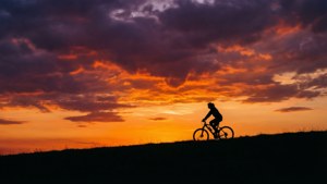 Une silhouette d'un cycliste au sommet d'une colline au coucher du soleil avec des couleurs dramatiques.