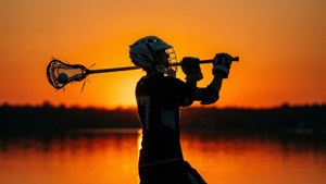 Silhouette d'un joueur de lacrosse devant un lac doré au coucher du soleil