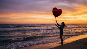 En person slipper en hjerteballon løs ved solnedgang på en strand.