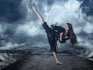 Uma mulher em uniforme preto de artes marciais chuta alto em um caminho de paralelepípedos perto de ondas oceânicas tempestuosas. — Taekwondo Papéis de Parede