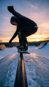 Peseluncur salju melakukan tailpress di atas rail saat matahari terbenam dalam slopestyle.