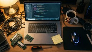 Et rodet overhead flat lay af et pc-skrivebord med komponenter, kaffe og klistermærker.