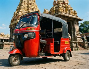 Sebuah becak motor merah dengan detail vintage di depan kuil yang dihiasi.