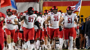 Texas Tech football team running onto the field at night with flags.