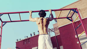 Mann macht Klimmzüge an Außenbar mit tätowiertem Rücken — Fitness Wallpaper