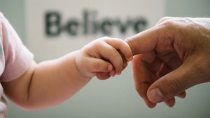 La main d'un enfant avec un parent, fond d'écran chaleureux avec texte 'Believe' caché