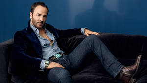 Homem de blazer de veludo e jeans relaxando em um sofá escuro contra uma parede azul. — Fashion Papéis de Parede