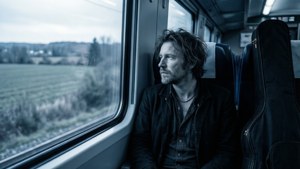 Beck Hansen di kereta melihat ke luar jendela dengan kotak gitarnya di sampingnya