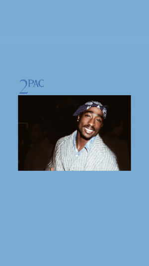 Porträt von 2Pac lächelnd in gestreiftem Hemd und Bandana mit blauem Hintergrund und Text.