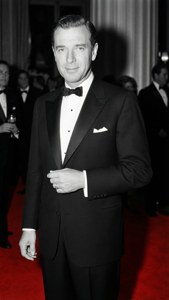 Elegante foto en blanco y negro de William Haines con un esmoquin a medida en una alfombra roja, con sombras dramáticas y pose clásica de Hollywood.