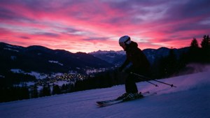 Bermain ski yang tenang di senja dengan langit berwarna-warni dan lampu desa yang jauh.
