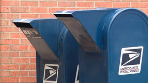 Deux boîtes aux lettres bleues du Service Postal des États-Unis aux rabats ouverts contre un mur de briques.