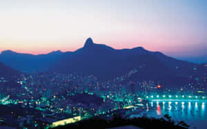 City lights reflect on water as mountains rise against a twilight sky. — Nature Landscape Picture