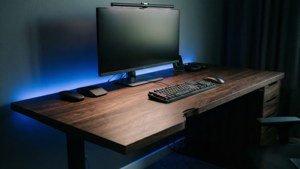 Scrivania moderna a L in noce scuro con monitor e atmosfera LED blu.