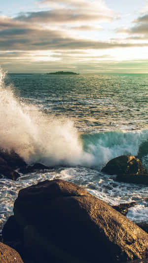 Waves crash against rocks at sunset with an island in the distance. — Wave iPhone Picture