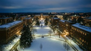 Rauhallinen panoraamanäkymä lumisesta yliopistokampuksesta valaistuna yöllä.