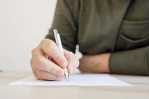 Hand holding pen writing on paper at wooden desk — Writing Background