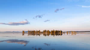 Lago calmo refletindo árvores e montanhas nevadas sob um céu azul com nuvens. — Lago Papéis de Parede
