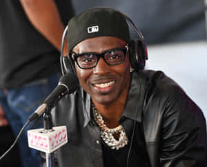 Man in black cap and leather jacket smiling at microphone in radio studio. — Rapper Wallpaper